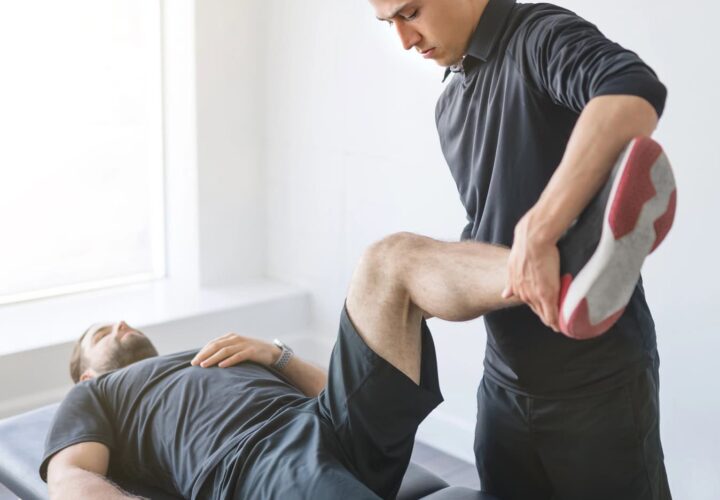 A Physical Therapy Clermont specialist stretches a patient's leg while the patient lies on an examination table in a bright room.