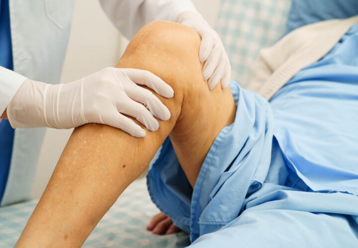 Medical professional wearing gloves examines a patients knee while the patient lies on a hospital bed.